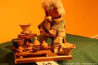 Wooden figurine of a potter with beard seated at a potter's wheel with miniature pottery items around.