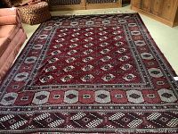 Full view of deep red geometric Persian rug on light carpeted floor.
