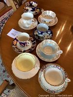 Overview of eight assorted tea cup and saucer sets arranged on wooden table