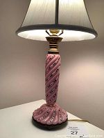 Full side view of pink glass lamp lit with fabric shade on.