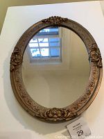 Full view of the oval antique gold wooden mirror showing reflective glass and ornate floral carvings on the frame.