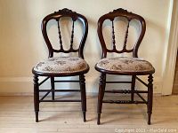 Full front view of both antique balloon back chairs showing carved shell patterns and floral upholstery