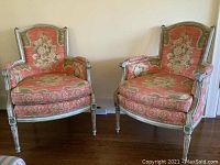 Two painted wood trimmed upholstered chairs with floral fabric against wall on wood floor