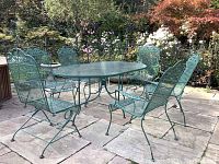 Full set: oval table and six chairs on stone patio, two chairs with coil springs visible at front.