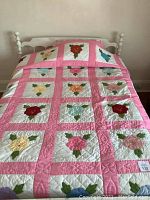 Full view of the quilt laid on a double bed showing its overall pattern of pink border and white squares featuring multicolored flower appliques.