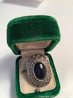 Top view of sterling silver ring set in green velvet box showing oval black onyx cabochon surrounded by scalloped marcasite-set bezels