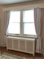 Full view of pair of white curtains with pink trim hanging on window, tied back with pink tassel ropes.