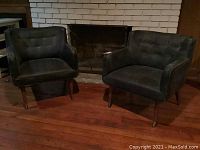 Two black lounge chairs side by side in front of fireplace on hardwood floor