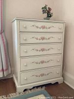 Front view of the vintage white chest featuring five drawers with floral stencil decoration in pink and green.