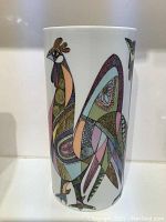 Front view of the tall cylindrical vase with multicolor psychedelic bird art on white ceramic surface.