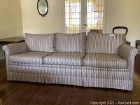 Full frontal view of the sofa showing its three cushions, striped fabric pattern and rolled arms with skirted base.