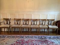 Six walnut dining chairs lined up against wall