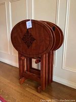 Four oval wooden TV trays nested in stand against wall