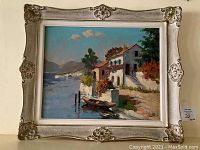 Full view of framed oil painting showing lakeside village scene