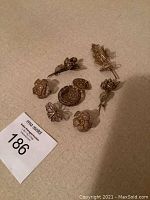 Six gilt silver brooches and one round pill box displayed on a beige surface, showing overall lot contents.