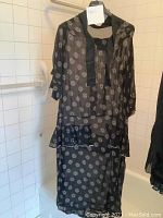 Full front view of navy chiffon dress with white print hanging in tiled bathroom