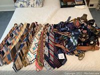 Two groups of vintage men's ties laid side by side on white quilted bedding, showcasing diverse colors and patterns including stripes, plaids, and floral designs.