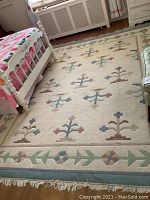 Full view of the wool area rug in a room, showing cream background and pastel floral motifs with fringe edges.