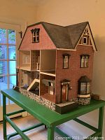 Front and side view of large red brick-style dollhouse on green wheeled table