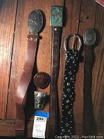 All four belts and two loose buckles laid out on wooden surface.