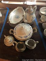 Overview of teapot, covered serving dish, creamer, sugar bowl, and platters showing blue floral decoration on cream background.