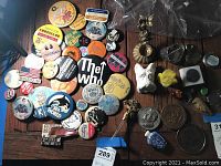 Overview of pinback buttons and small collectibles including metal and ceramic items on dark surface.