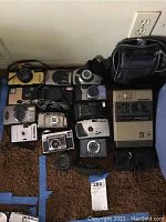 Lot of multiple cameras laid out on carpet including brands Nikon, Kodak, Polaroid, Bell & Howell, Ricoh