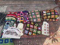 Lot of various crochet blankets including colorful granny square designs and a cream-colored crochet vest.