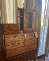 Wide shot showing large wooden jewelry chest with brass hardware, small wooden box, and wooden display cabinet with glass door and side shelving.