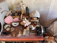 Overview of workbench with polishing motor, box of rough stones, geode halves, shells and coral