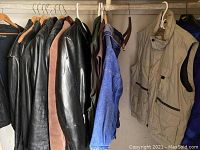 Multiple leather jackets hanging on hangers showing a variety of black and brown leather jackets as well as other outerwear.