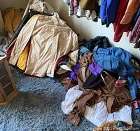 Photo showing a pile of men's shirts and jackets in various colors including beige and mustard yellow, laid on a floor.