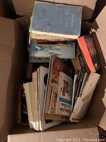 Box filled with mostly vintage books and magazines, showing an assortment of titles and formats from top view inside box.