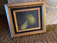 Photo of framed still life painting featuring a lemon and a lemon wedge on a dark background, showing detail of the painting and frame