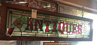 Front view of rectangular stained glass sign with 'ANTIQUES' text in red and floral motifs on each side.