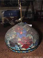 Side view of dome-shaped stained glass lamp with floral mosaic pattern on a brown carpet.