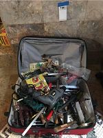 Photo showing a variety of hand and power tools mixed in a suitcase, including a visible power drill, wrenches, and clamps.