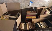 Wide view of boxes filled with vintage books and magazines stacked on a desk, showing the quantity and condition of the lot.