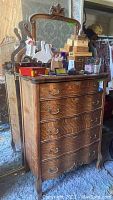 Front view of vintage wooden dresser with mirror showing five curved front drawers with metal handles and ornate carved crest on mirror frame.