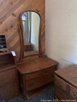 Full view of the vanity dresser showing the tall attached mirror with rounded top and supports, the curved front of the dresser, and the wood finish.