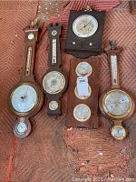 Four vintage wooden wall-mounted weather stations with various dials for measuring temperature, air pressure, and humidity on a textile surface.