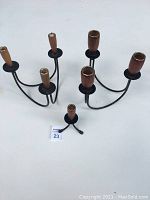 Photo showing two triple candle holders with black metal frames and wooden candle cups, and one smaller single candle holder with three feet and wooden cup in front