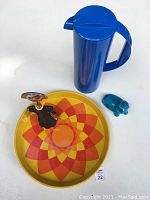 Lot showing Alessi bottle opener, Rosti blue pitcher, yellow tray with orange and red geometric pattern, and turquoise Bitossi hippo figurine.