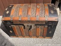 Front view showing arched lid, wood slats, embossed tin panels and central hasp lock