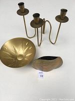 Photo showing all three items together: brass vase with patina, hammered bowl with leaf design, and three-arm brass candle holder.