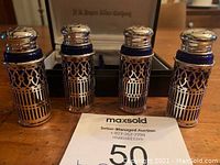 Four vintage style purple glass shakers with silver plated lattice holders and tops placed upright on wooden surface with box behind them