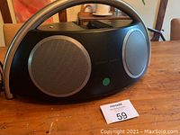 Front view of the Harman Kardon Go+Play black portable speaker with dual speakers and handle, placed on a wooden table with auction tag 59 in front.