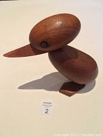 Angled side view of wooden duck sculpture showing smooth rounded head, body and pointed beak.
