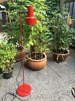 Full view of the red floor lamp standing outside on pavement, showing its design and color.