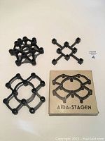 Three black iron candle holders arranged around an Aida-Stagen box on a white background